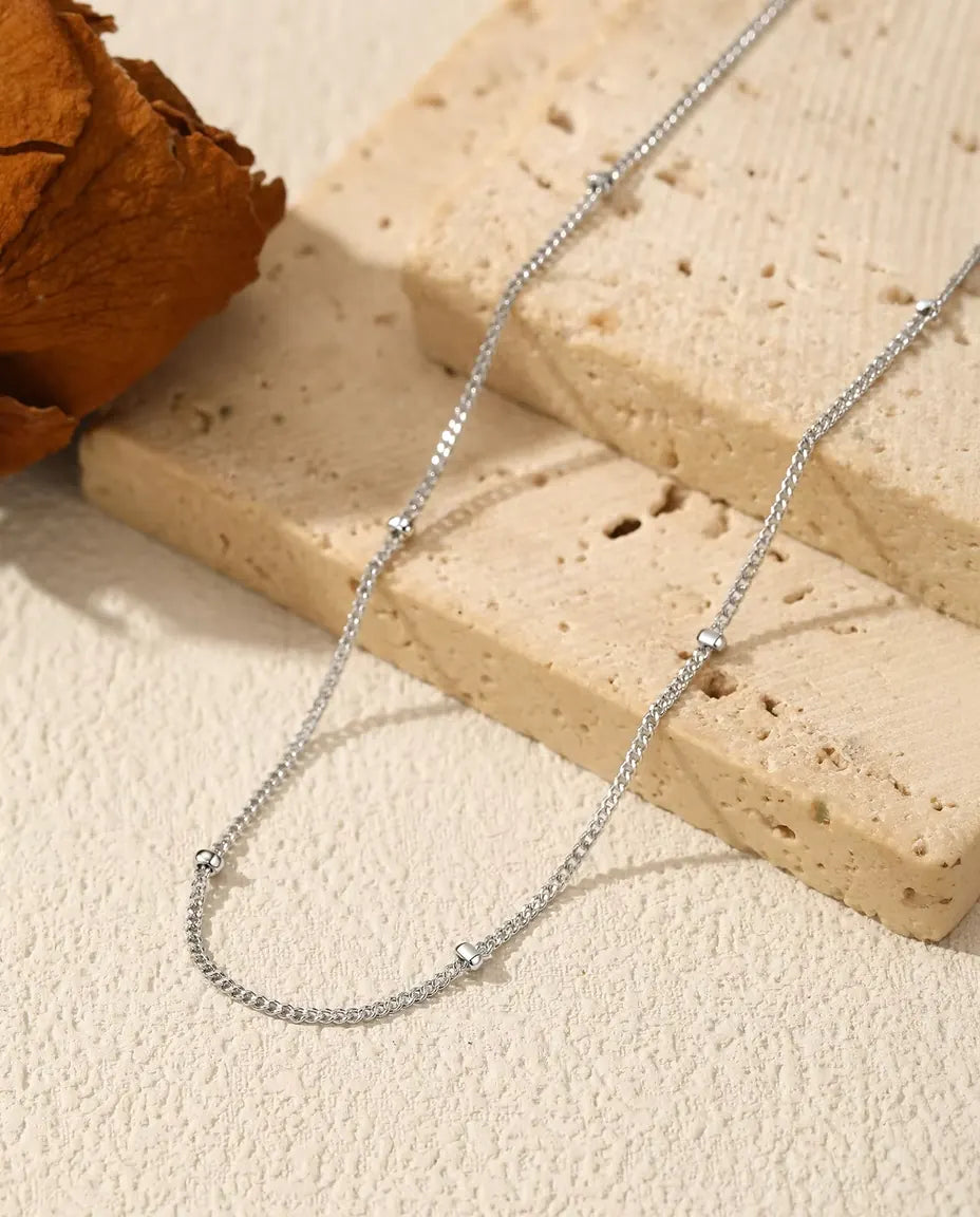 Satellite Chain Necklace in 925 Sterling Silver - draped across a cream surface beside a travertine slab
