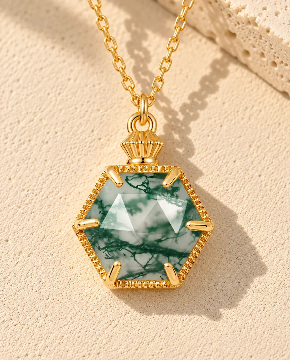 Hexagon Moss Agate Necklace in 10K Gold Plated 925 Sterling Silver - lying on a cream textured surface beside a travertine block
