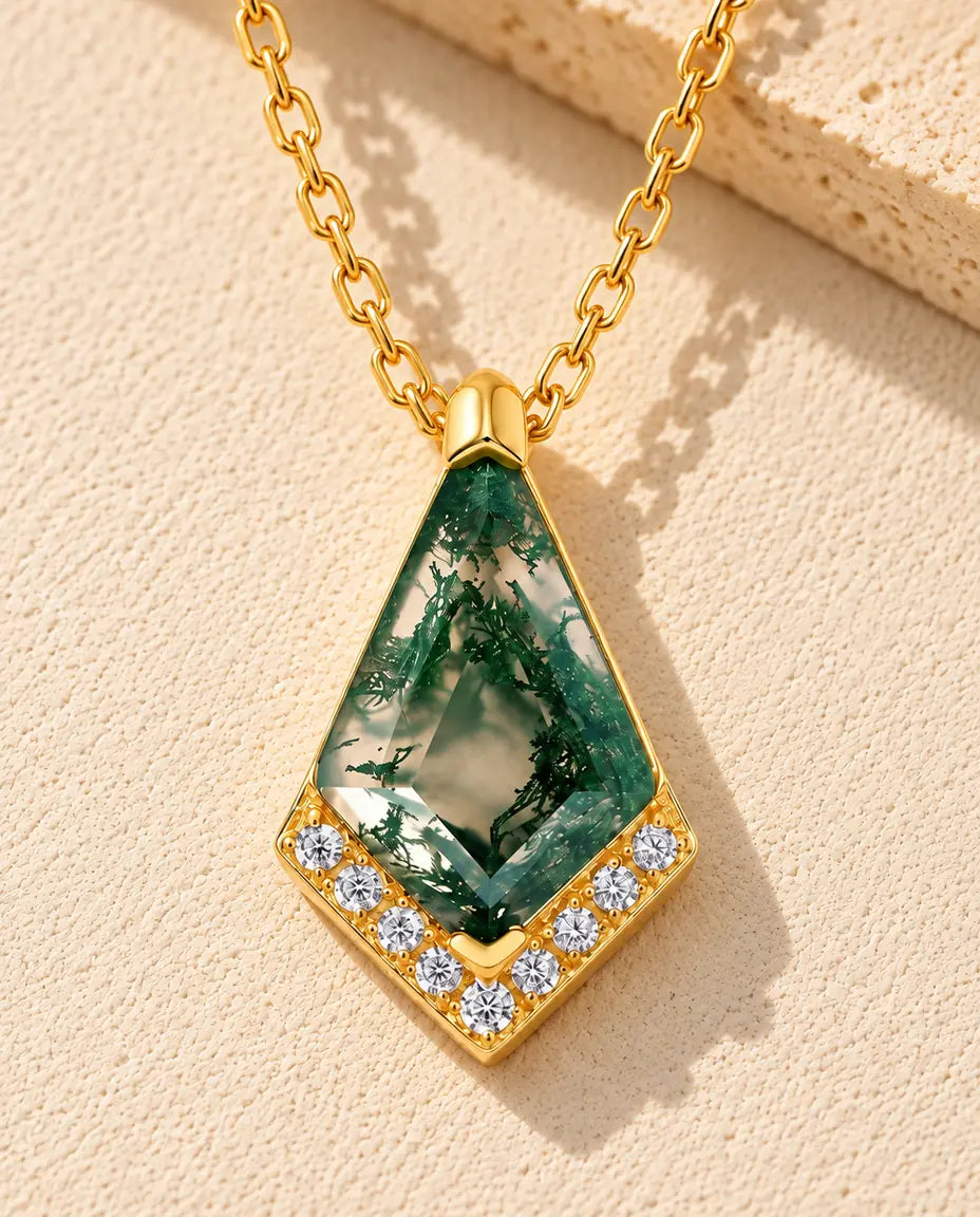 Kite Moss Agate Necklace in 10K Gold Plated 925 Sterling Silver - lying on a cream textured surface beside a travertine block