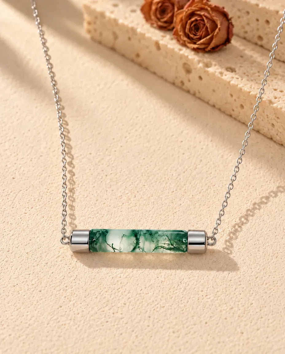 Moss Agate Bar Necklace in 925 Sterling Silver - lying on a cream textured surface beside a travertine block