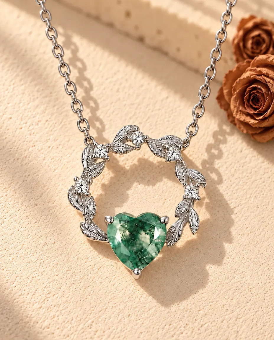 Moss Agate Heart Necklace in 925 Sterling Silver - lying on a cream textured surface beside a travertine block