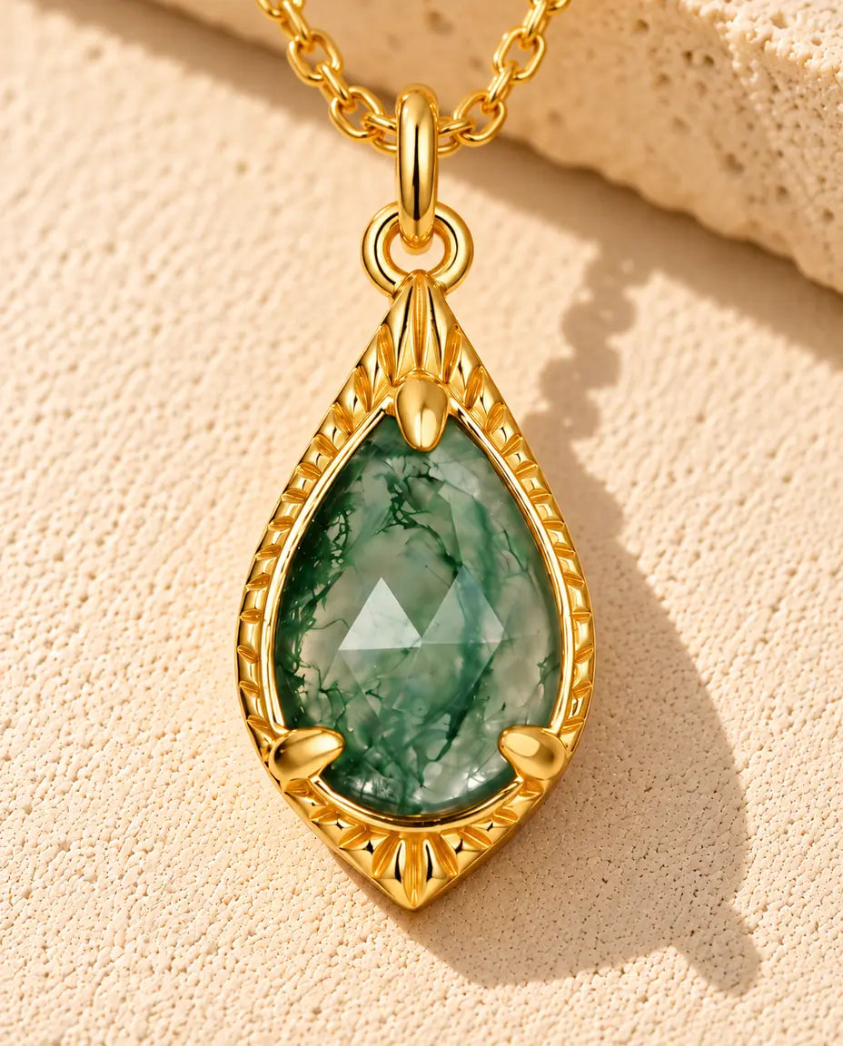 Teardrop Moss Agate Necklace in 10K Gold Plated 925 Sterling Silver - lying on a cream textured surface beside a travertine block