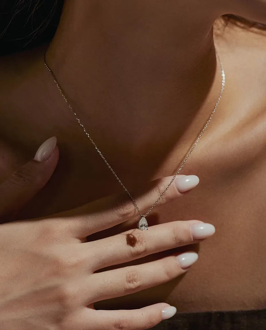 1 ct Pear Moissanite Necklace in 925 Sterling Silver - worn on a model with her hand at her neck