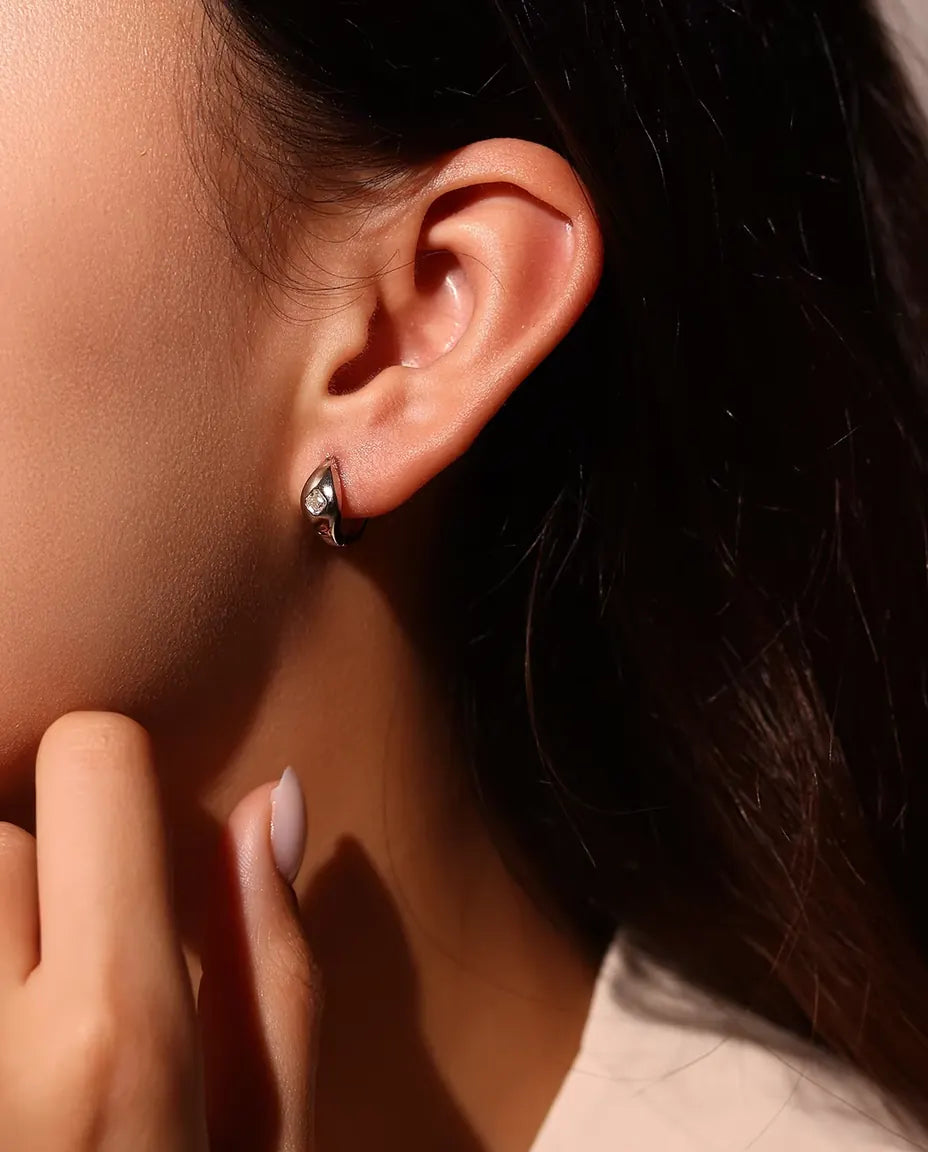 Asscher Cut Moissanite Huggie Hoop Earrings in 925 Sterling Silver - worn on a model’s ear, hand near her face