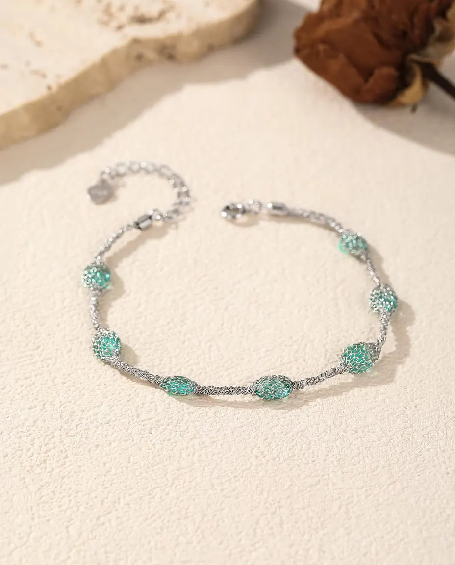Caged Zircon Bracelet in 925 Sterling Silver - green zircon version beside a travertine slab and a dried rose