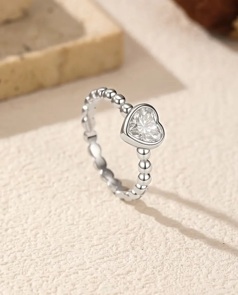 Heart Moissanite Ring in 925 Sterling Silver - standing upright on a cream textured surface