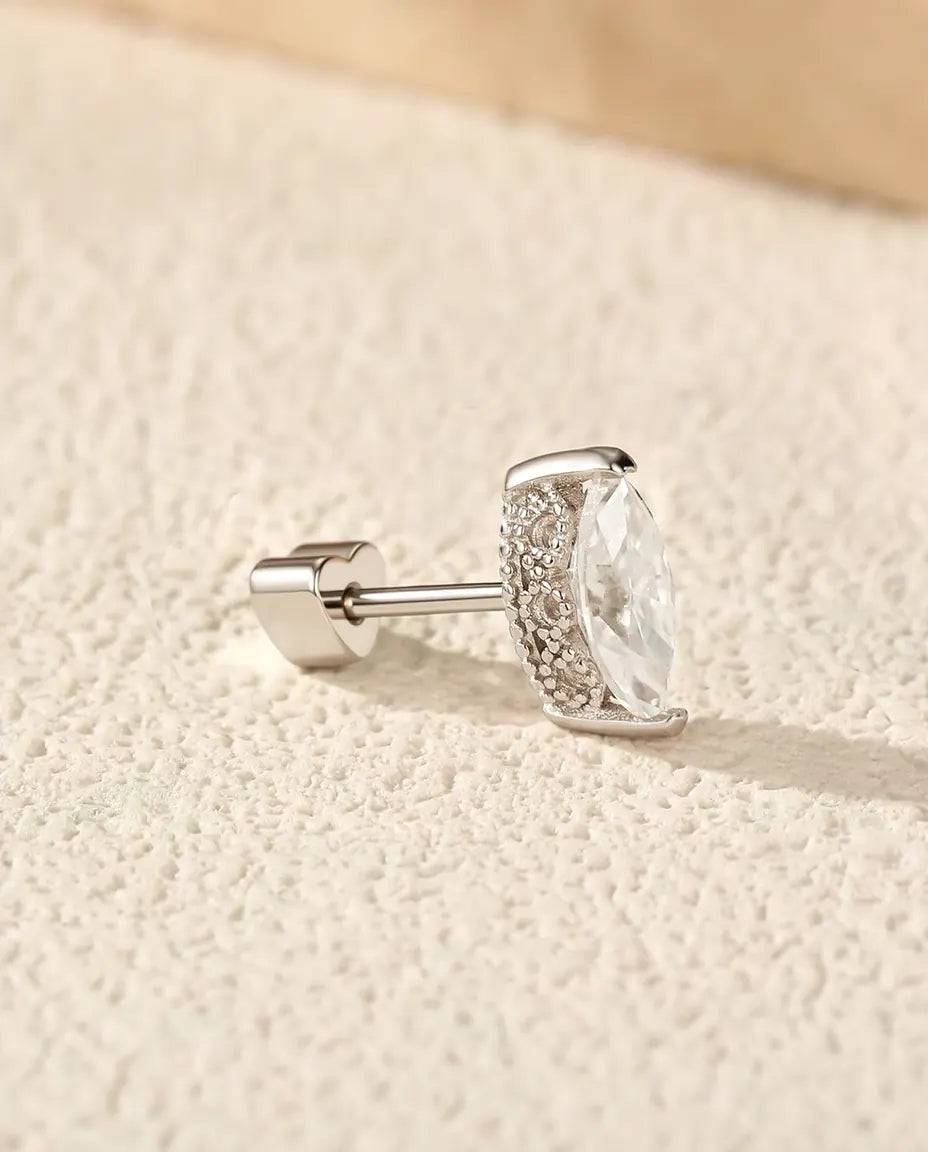 Marquise Moissanite Stud Earrings in 925 Sterling Silver - lying on a cream textured surface beside a travertine slab
