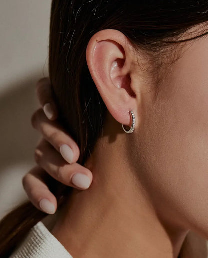 Moissanite Huggie Hoop Earrings in 925 Sterling Silver - worn on a model’s ear, hand holding back her hair