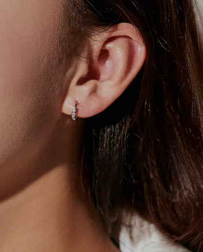 Moissanite Huggie Hoop Earrings in 925 Sterling Silver - worn on a model’s ear, close-up