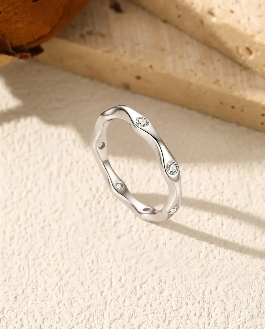 Moissanite Wave Ring in 925 Sterling Silver - standing upright on a cream textured surface