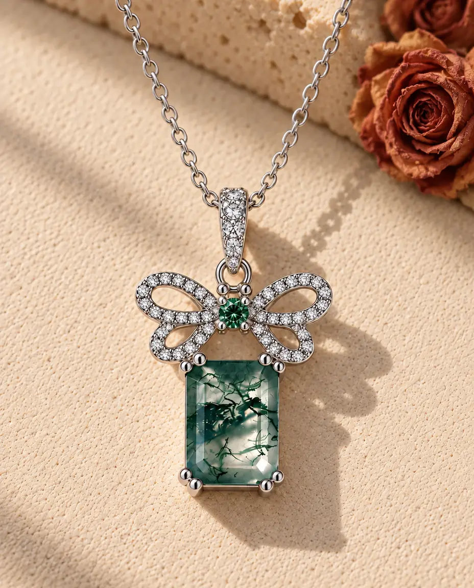Moss Agate Bow Necklace in 925 Sterling Silver - lying on a cream textured surface beside a travertine block