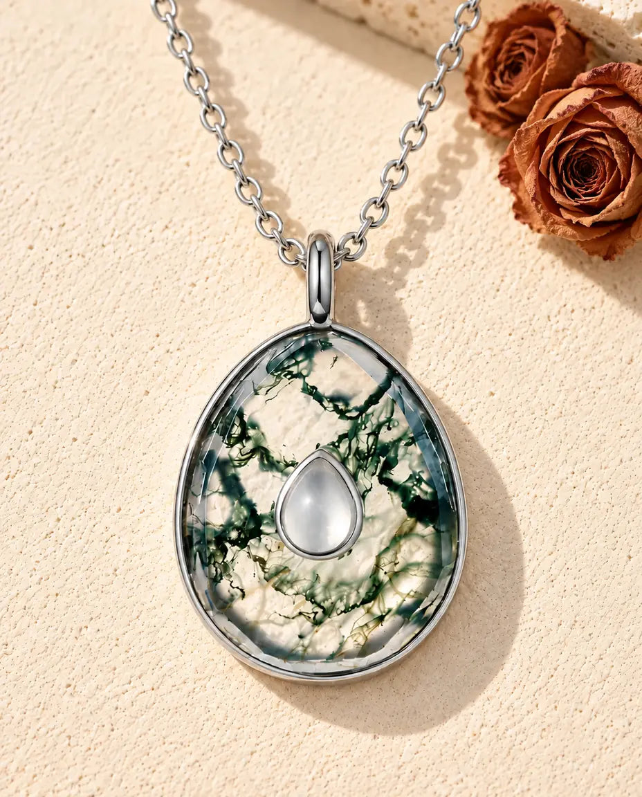 Moss Agate Egg Pendant Necklace in 925 Sterling Silver - lying on a cream textured surface beside a travertine block