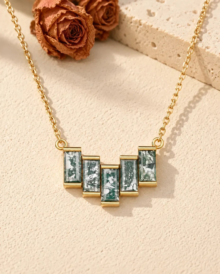 Moss Agate Baguette Necklace in 10K Gold Plated 925 Sterling Silver - lying on a cream textured surface beside a travertine block