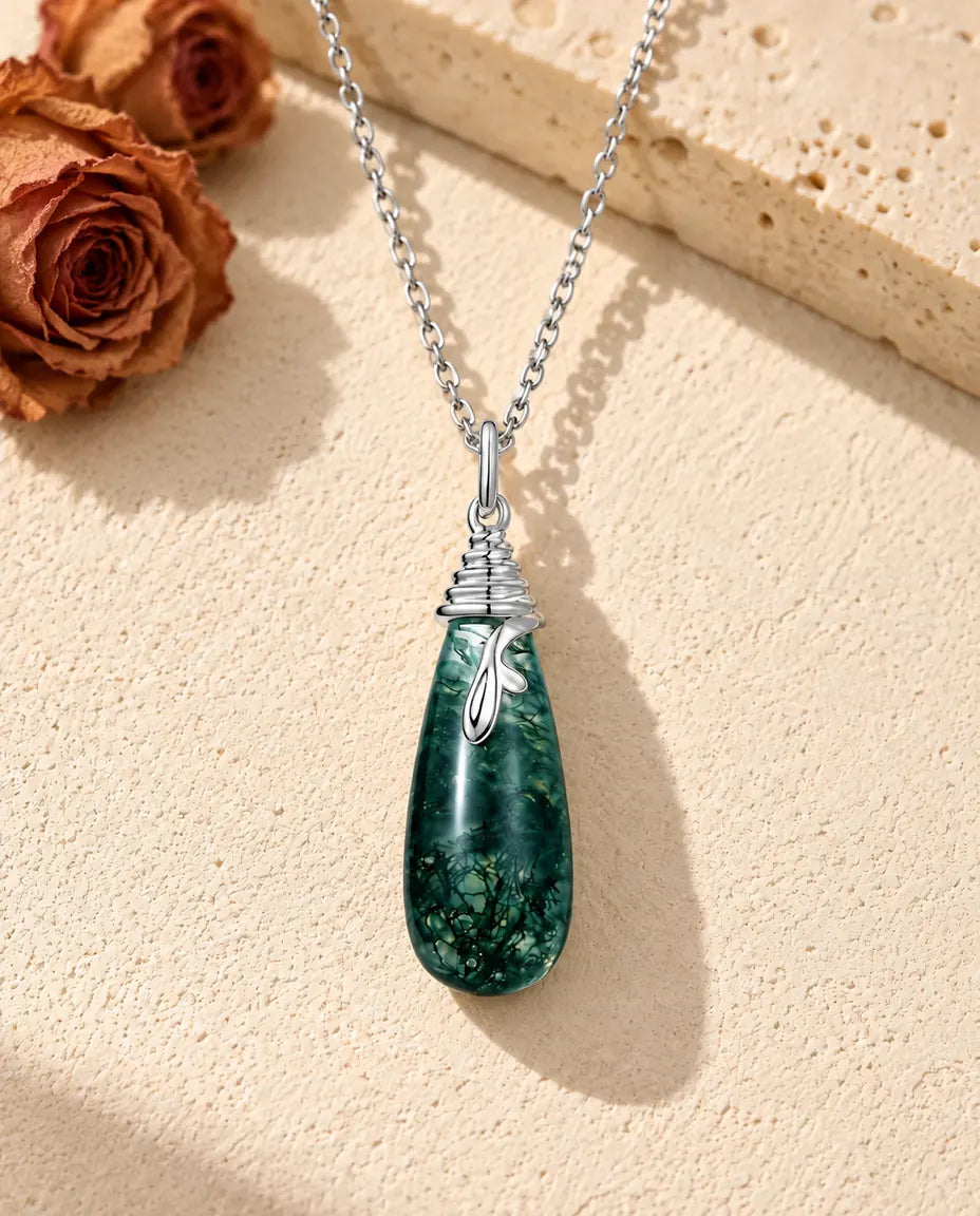 Moss Agate Teardrop Necklace in 925 Sterling Silver - lying on a cream textured surface beside a travertine block