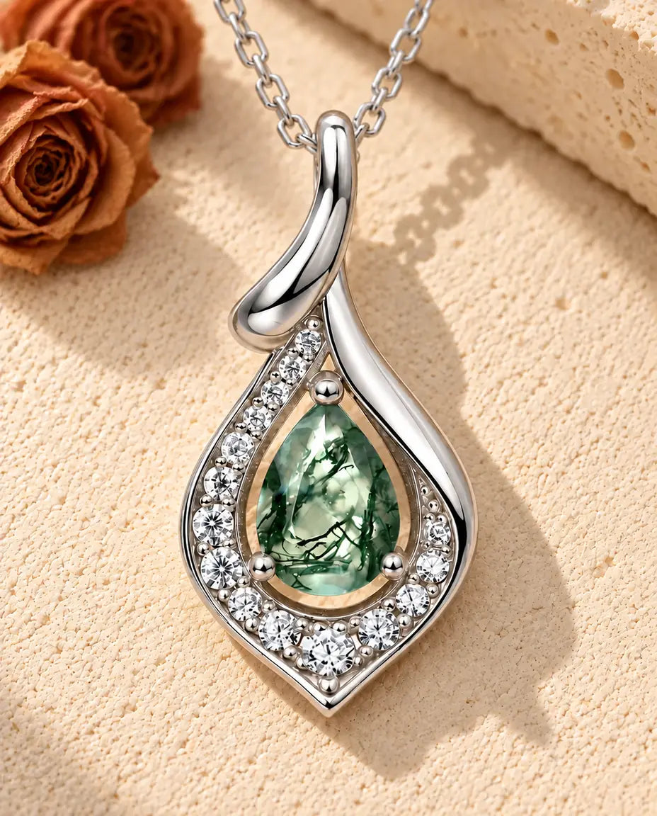 Pear Moss Agate Pendant Necklace in 925 Sterling Silver - lying on a cream textured surface beside a travertine block