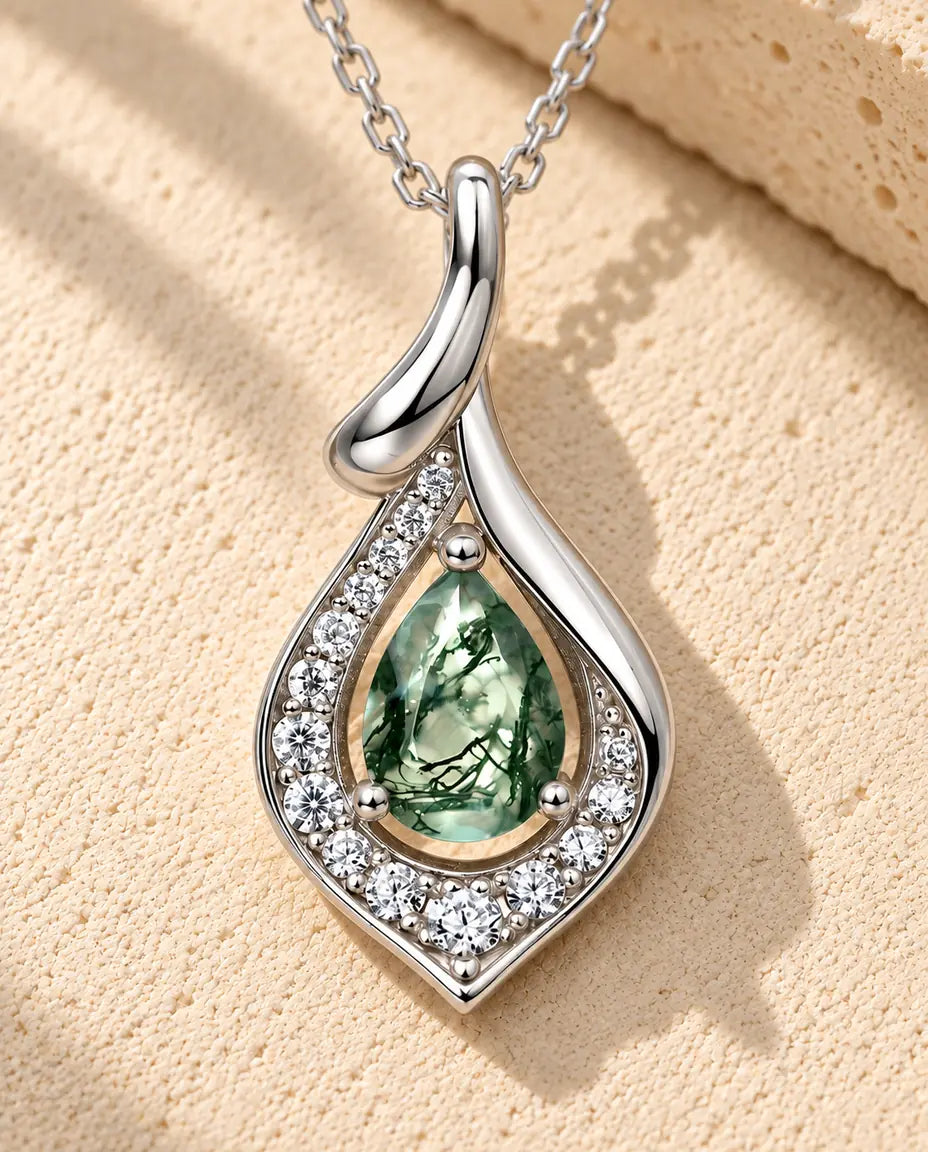 Pear Moss Agate Pendant Necklace in 925 Sterling Silver - lying on a cream textured surface beside a travertine block