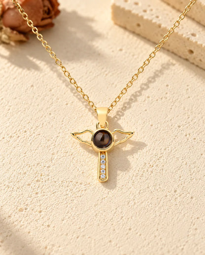 Front view of the gold tone cross with open angel wings and the projection stone at its centre