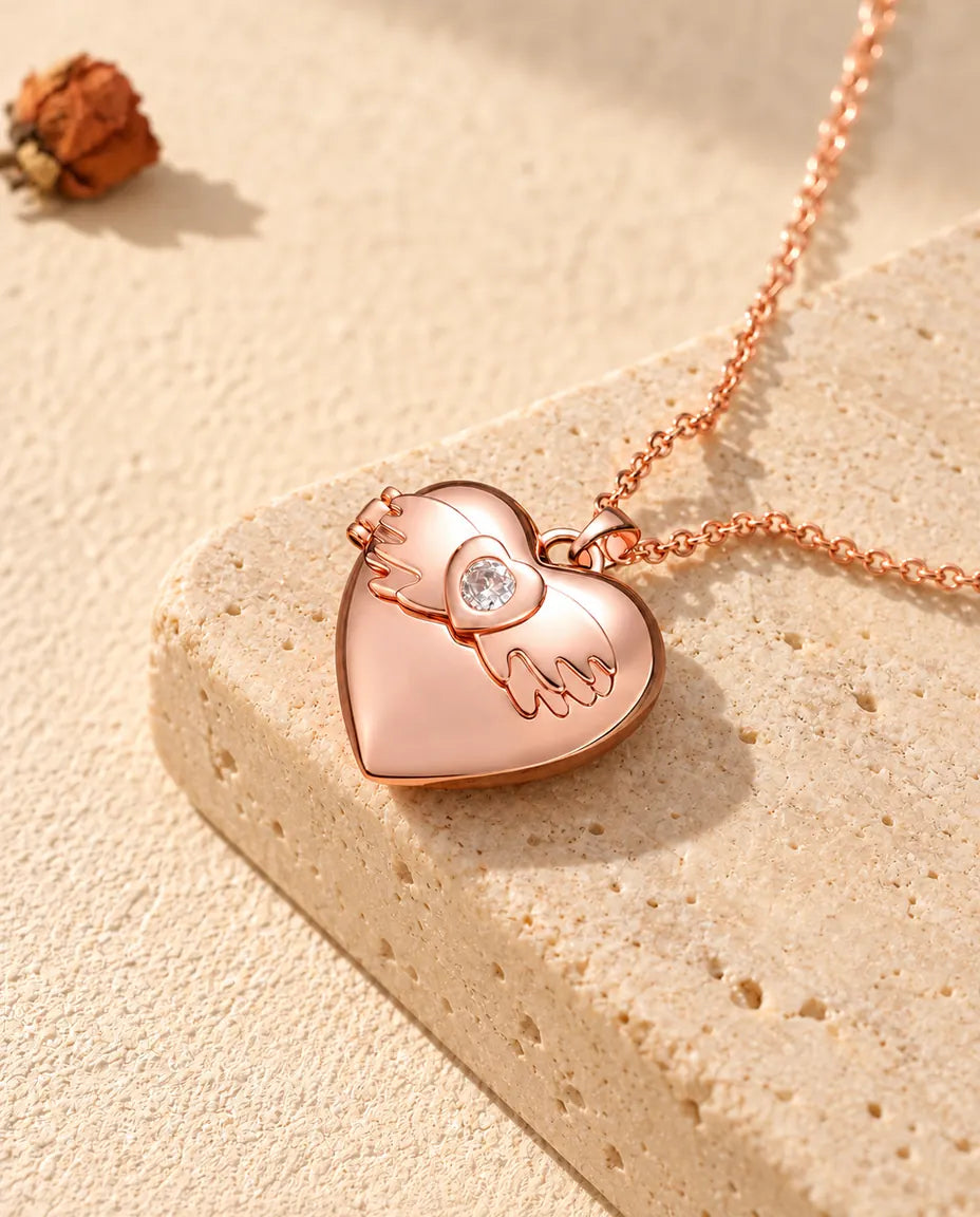 Rose gold tone angel wings heart photo locket necklace on travertine in warm sunlight