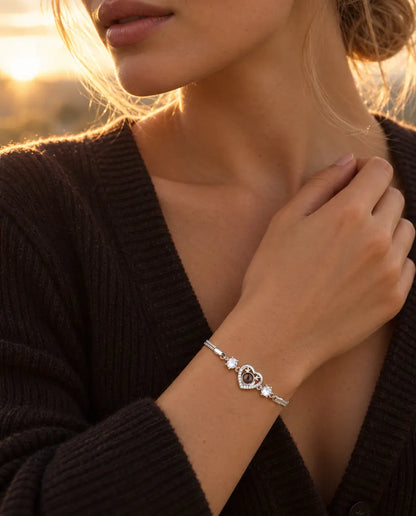 Woman touching the neckline of her dark knit top, wearing the silver tone antler heart projection bracelet