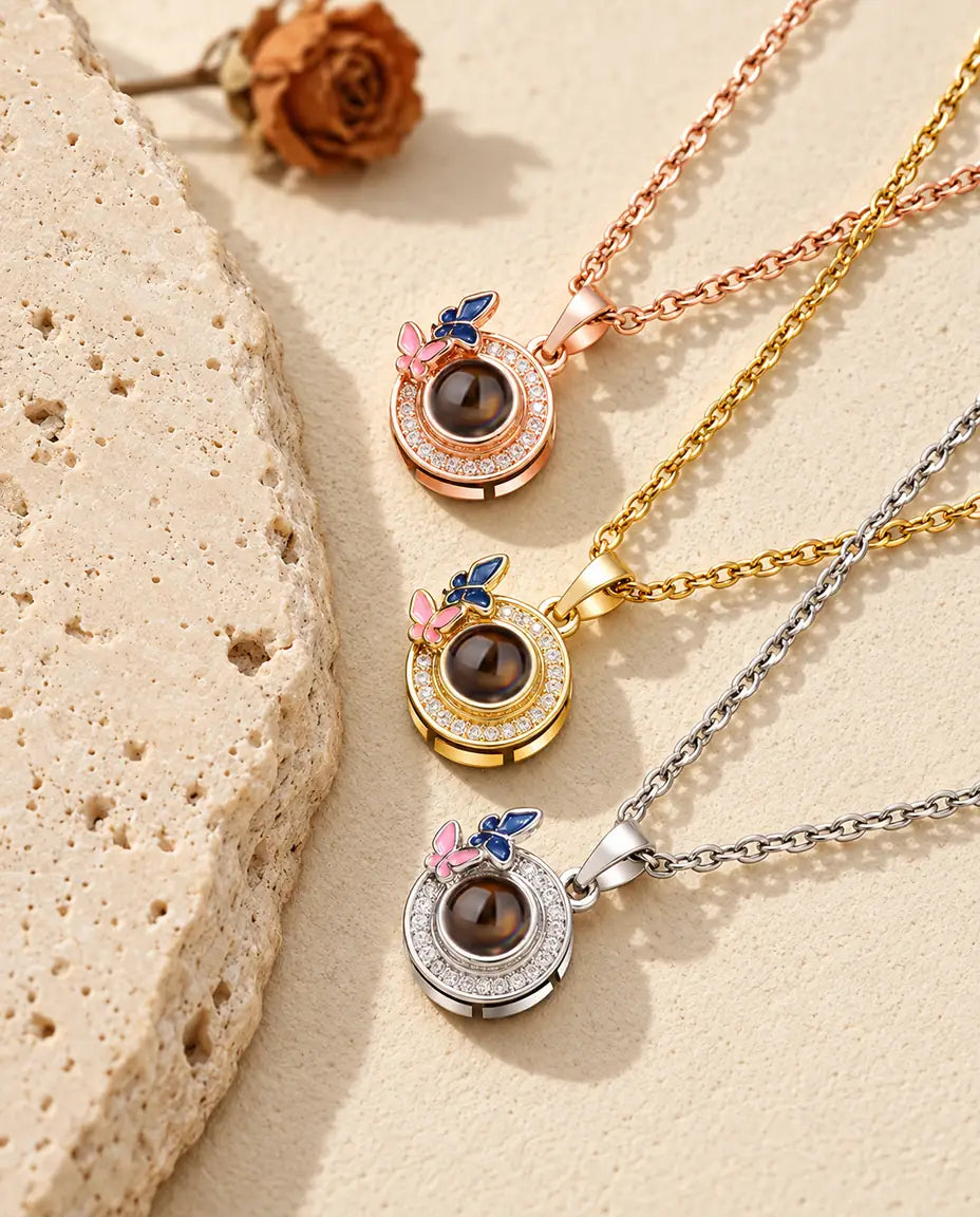 Rose gold tone, gold tone and silver tone butterfly circle pendants stacked beside a travertine slab