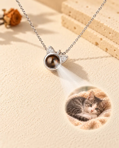 Silver tone cat ear necklace projecting a kitten photo onto cream plaster