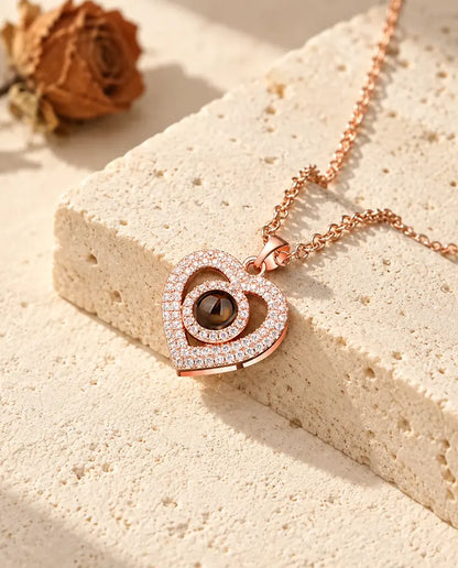 Rose gold tone double heart pave pendant resting against a travertine block