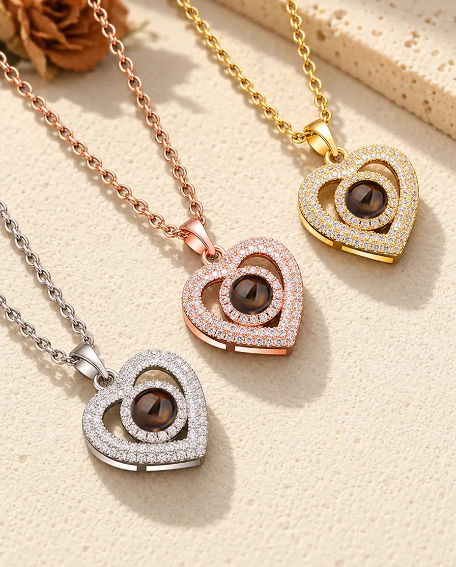 Three colours of the double heart photo projection necklace on a diagonal on cream plaster