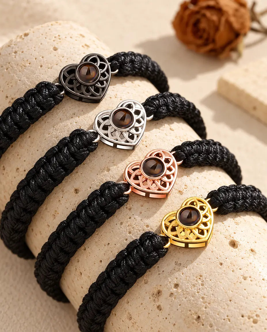 Four black braided cord bracelets showing every charm colour draped over travertine