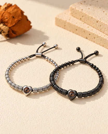 Personalised couples photo projection bracelets, a matching set of two heart bead bracelets in silver tone and black on cream plaster