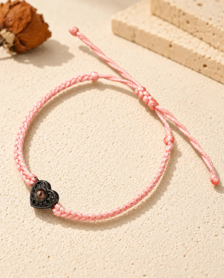 Pink thin braided cord bracelet with a black heart charm holding a brown projection stone