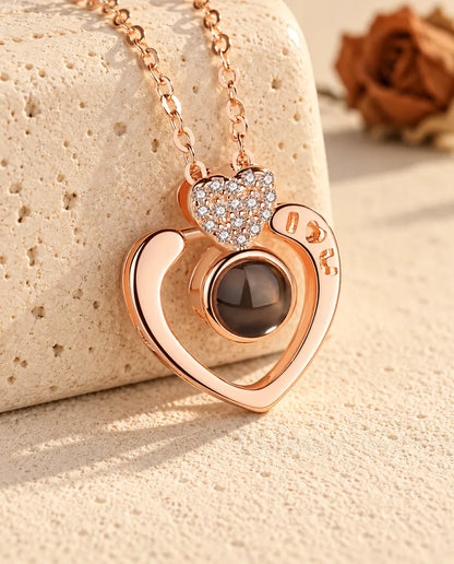 Personalised rose gold tone I love you open heart photo projection necklace resting on a travertine block