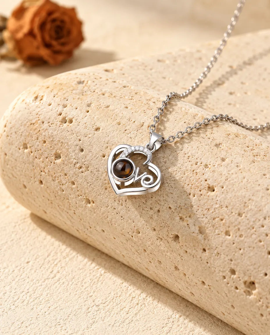 Personalised Love heart photo projection necklace in silver tone with a cubic zirconia arc, resting on a travertine block