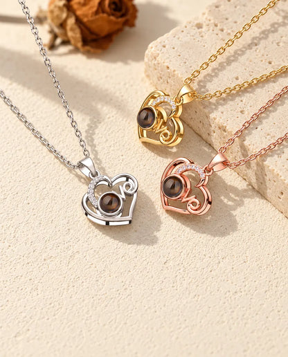 Love heart photo projection necklaces in silver tone, gold tone and rose gold tone beside a travertine slab