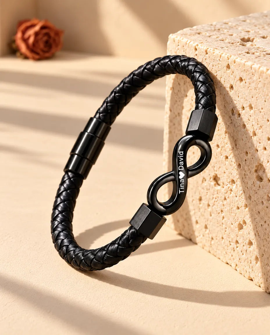 Black braided faux leather bracelet with an engraved infinity link standing against a travertine block