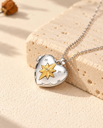 Personalised north star heart photo locket necklace in silver tone with a gold tone north star, resting on a travertine block