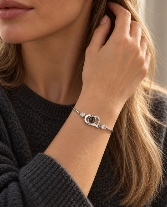 Woman with her hand in her hair, wearing the silver tone open heart projection bracelet