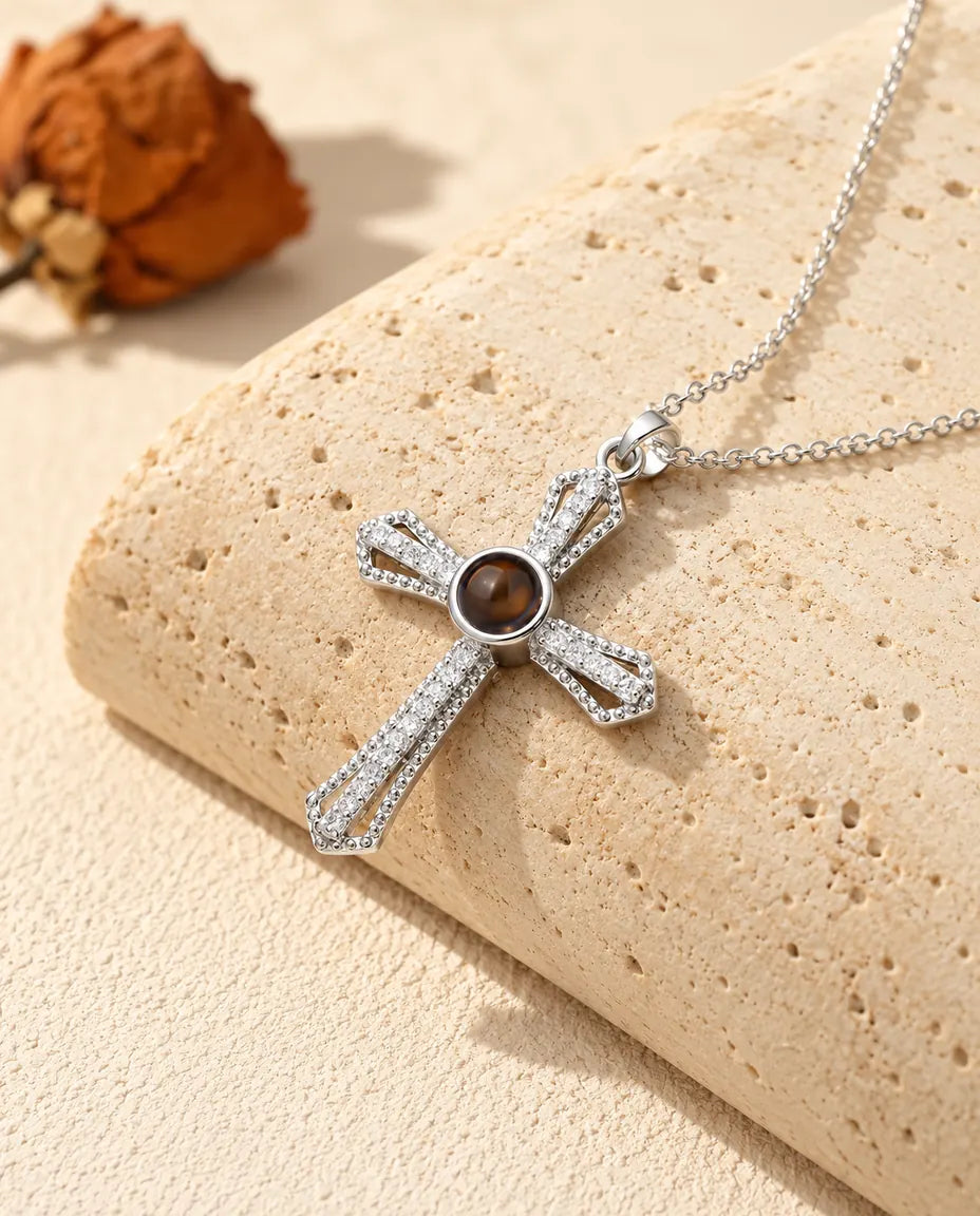 Personalised pave cross photo projection necklace in silver tone with a brown stone at the centre, on a travertine block