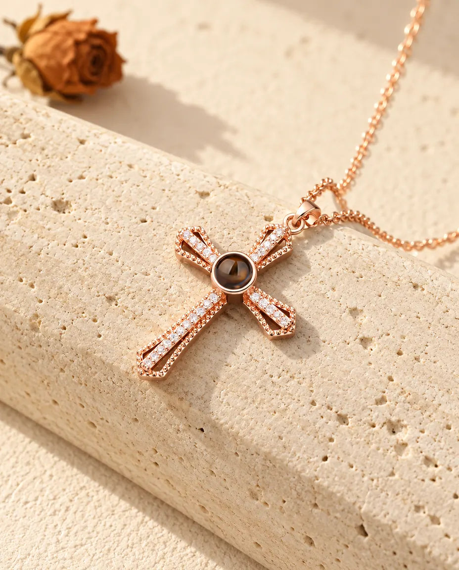 Rose gold tone pave cross necklace with a projection stone lying against travertine