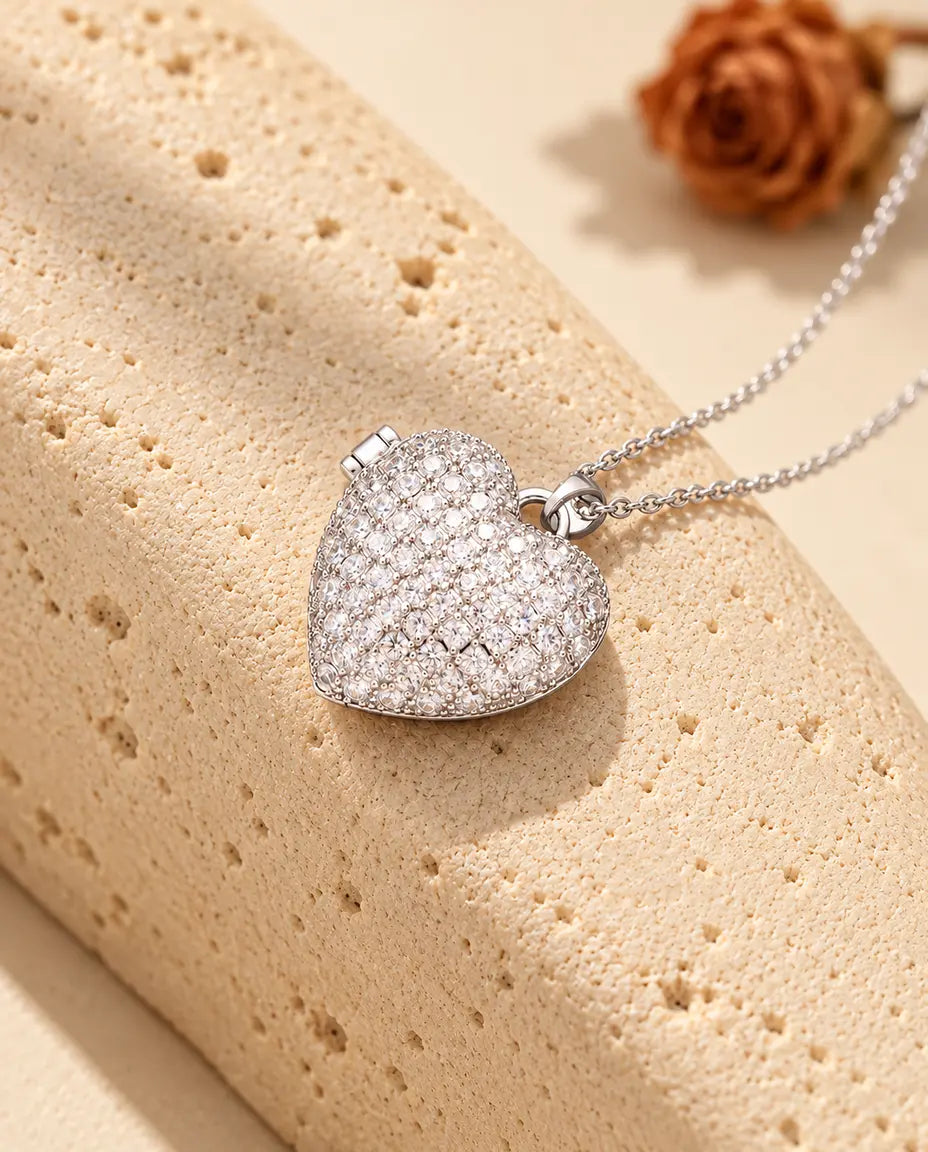Personalised pave heart photo locket necklace in silver tone covered in cubic zirconia, resting on a travertine block