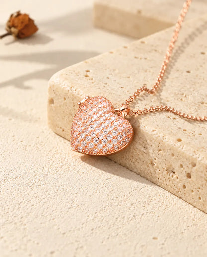 Rose gold tone pave heart photo locket necklace on travertine in warm sunlight