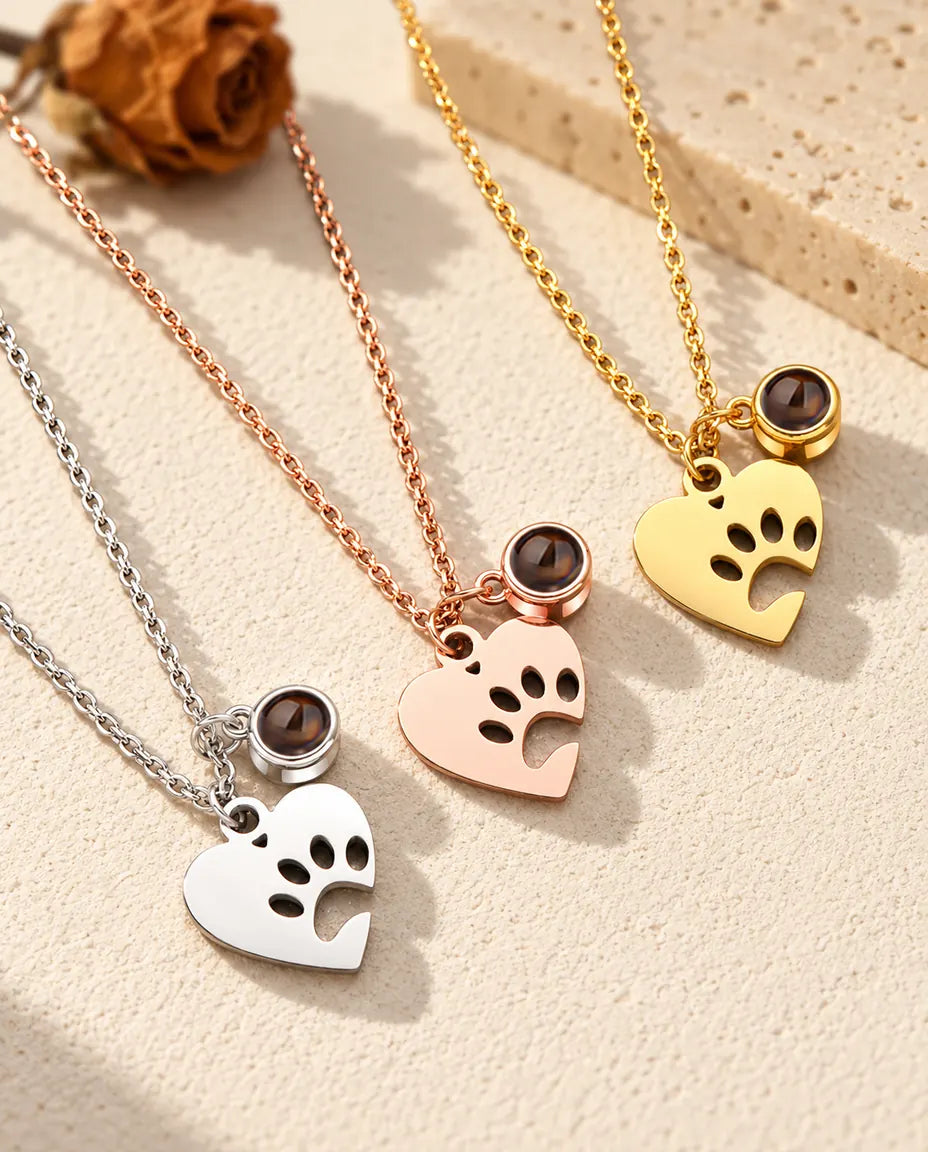 Three colours of the paw print heart pet projection necklace on a diagonal on cream plaster