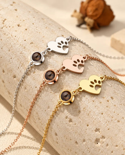 Three paw print heart projection bracelets in silver tone, rose gold tone and gold tone over a travertine block
