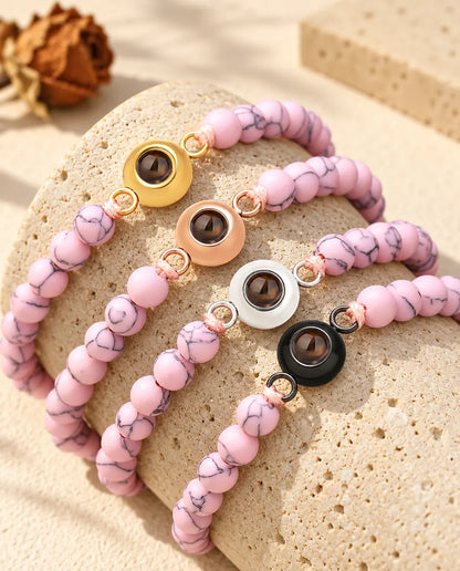 Pink marbled bead projection bracelets with four charm colours draped over travertine
