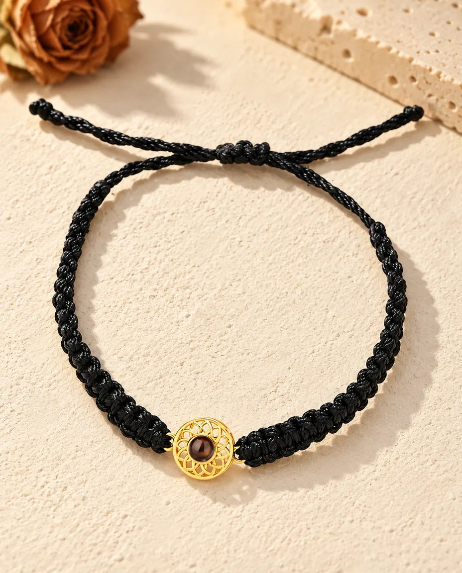 Top view of the gold tone round charm bracelet on a black braided cord with its sliding knot and cord ends