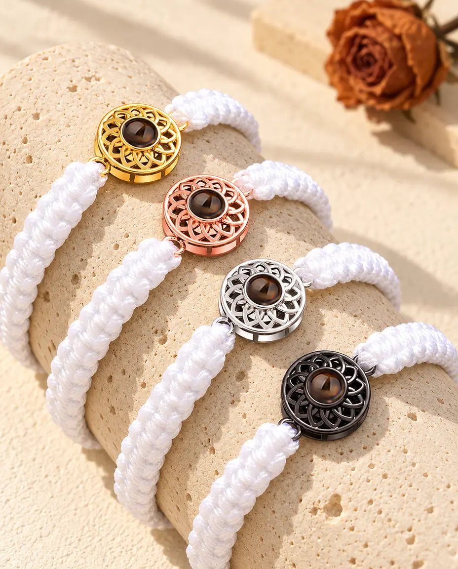 Four white braided cord bracelets with gold tone, rose gold tone, silver tone and black round charms on a travertine block