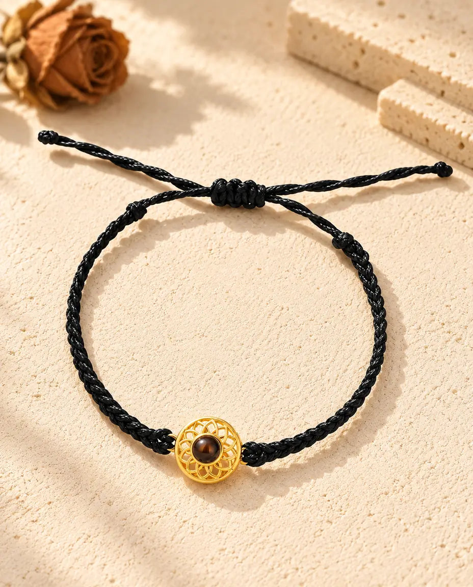 Top view of the gold tone round charm bracelet on a black thin braided cord with its sliding knot and cord ends
