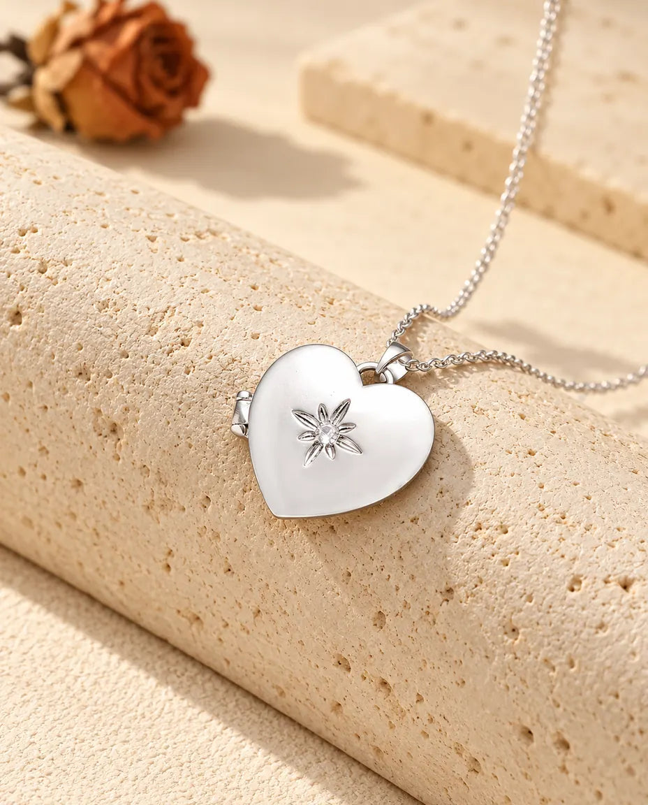 Personalised satin flower heart photo locket necklace in silver tone with a small starburst flower, resting on a travertine block