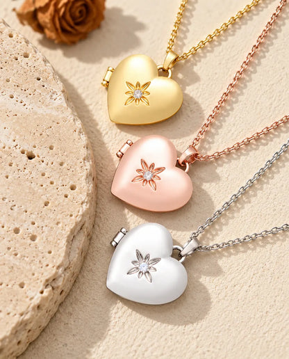 Gold tone, rose gold tone and silver tone satin flower heart photo lockets stacked beside a travertine slab