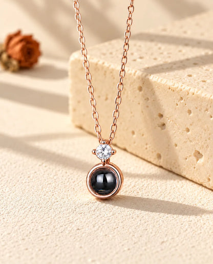 Rose gold tone solitaire projection necklace hanging in front of travertine