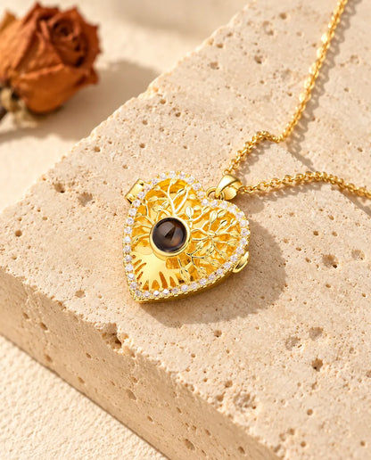 Gold tone heart locket with an openwork tree of life and a cubic zirconia outline resting on travertine